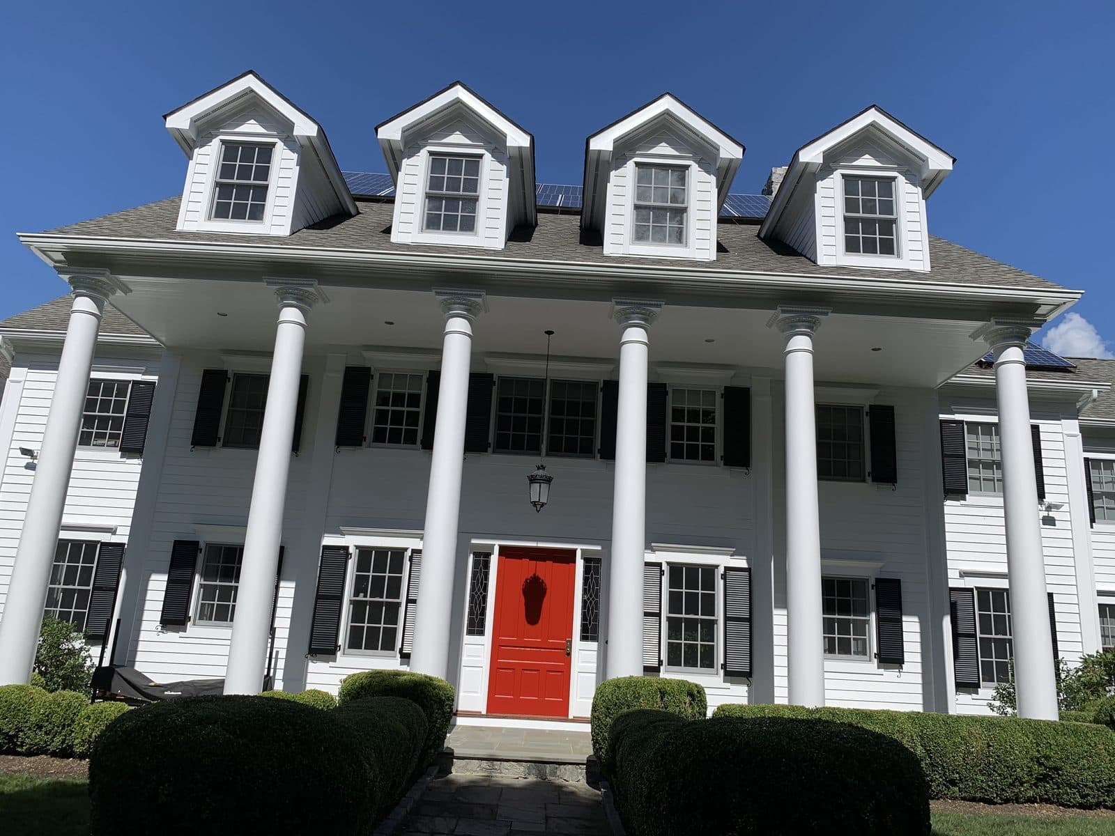 A beautifully painted white colonial home with a bold red door by C&C Fabian.