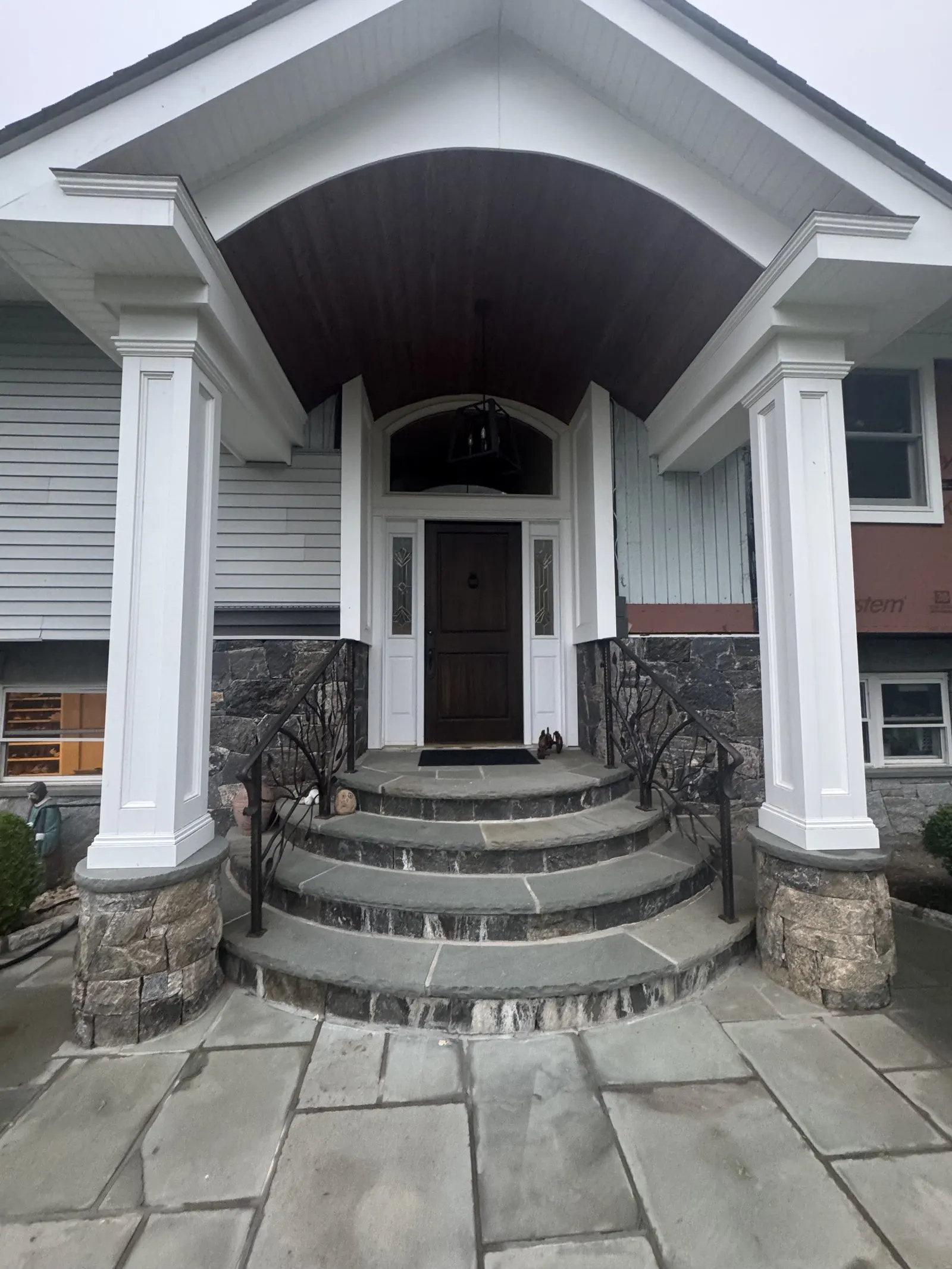 Completed home with a new columned portico, gray siding and stone entry steps