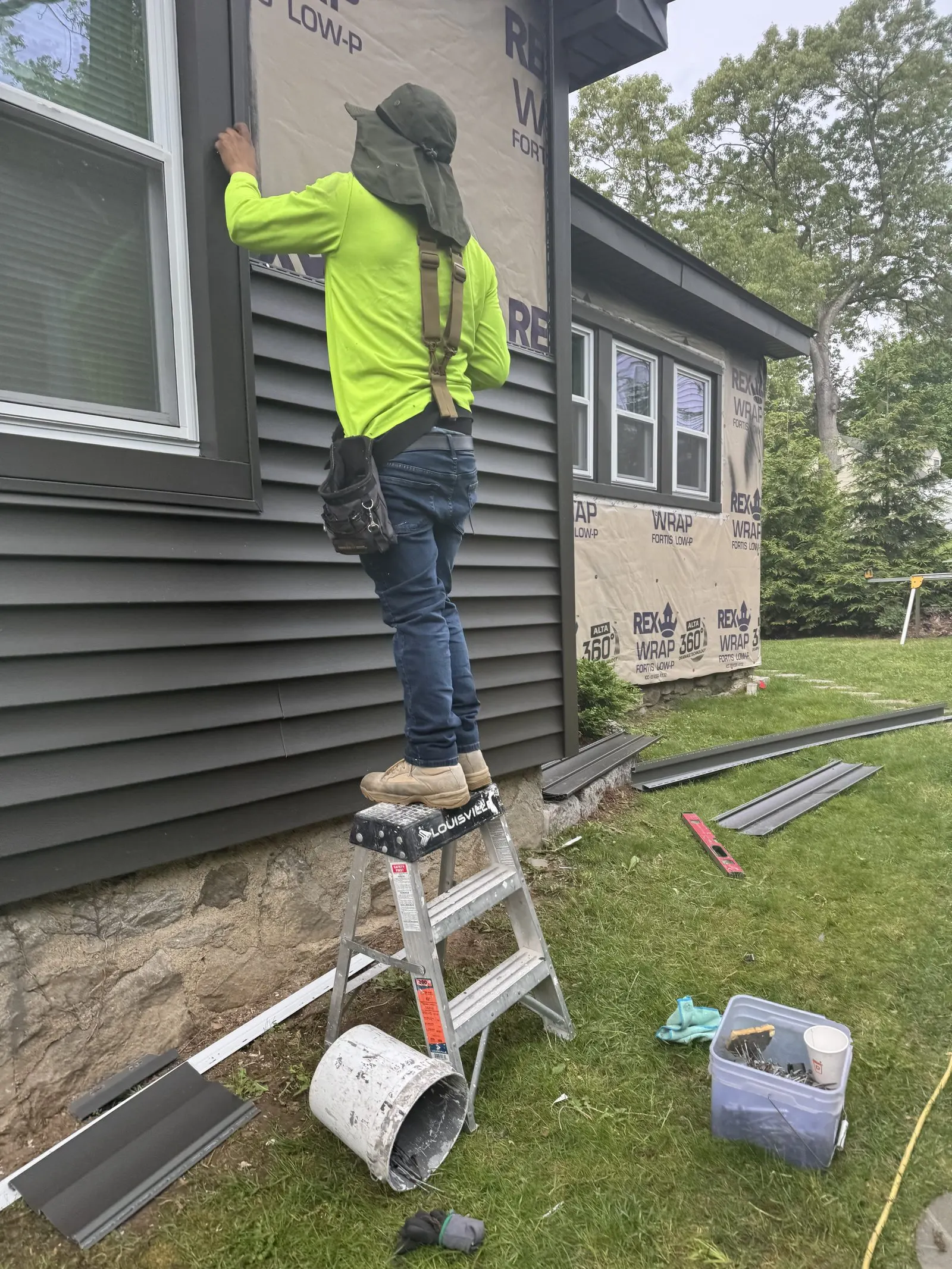 Crew member installing gray vinyl siding from a ladder