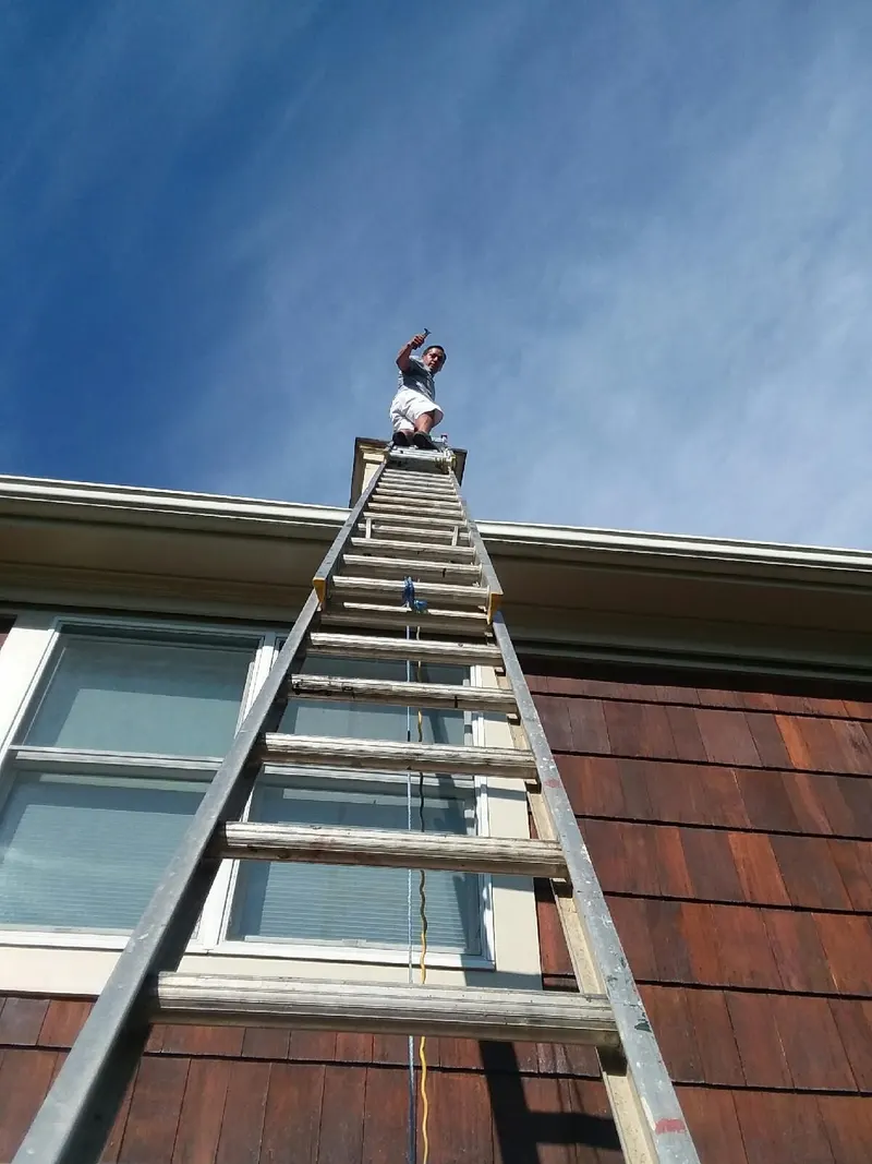 Crew member atop an extension ladder cleaning cedar shingle siding