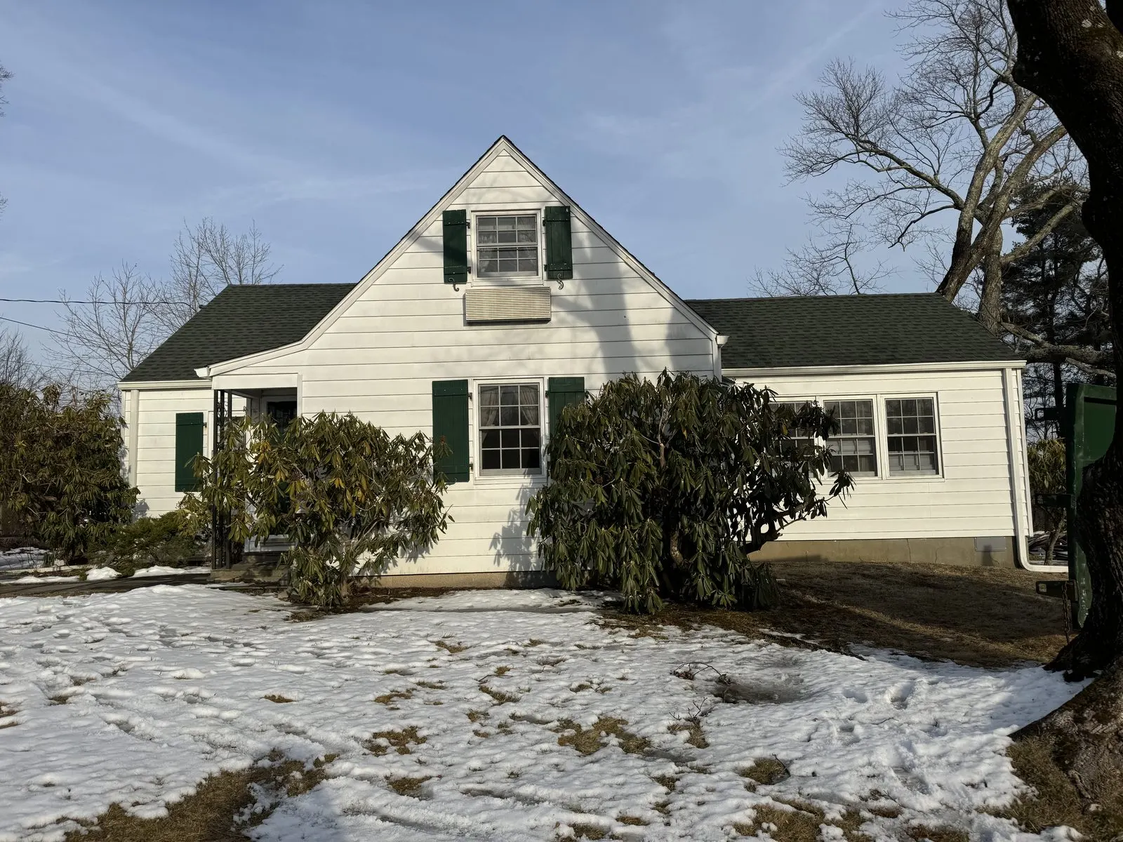 White cape home with green shutters before new siding