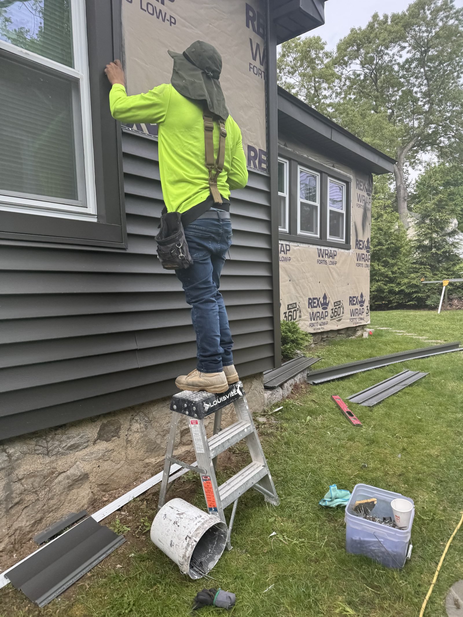 Crew member installing gray vinyl siding from a ladder